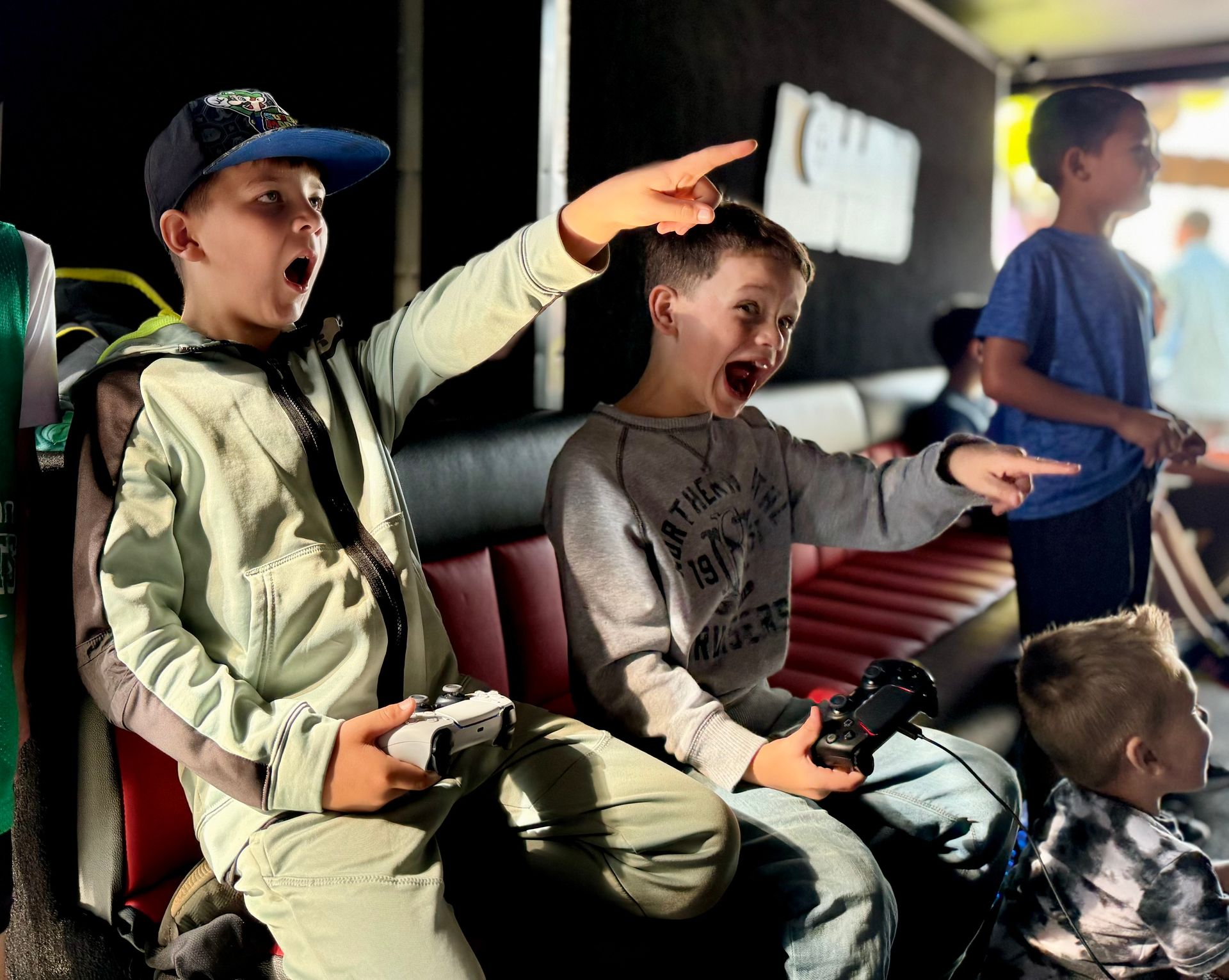 Three people playing a video game on a couch, showing excited expressions and pointing towards a screen.
