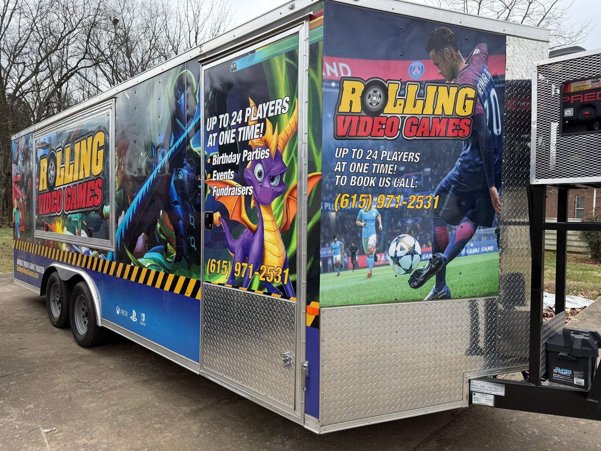 A Rolling Video Games trailer featuring colorful game graphics, including a purple dragon, displayed on a silver trailer.