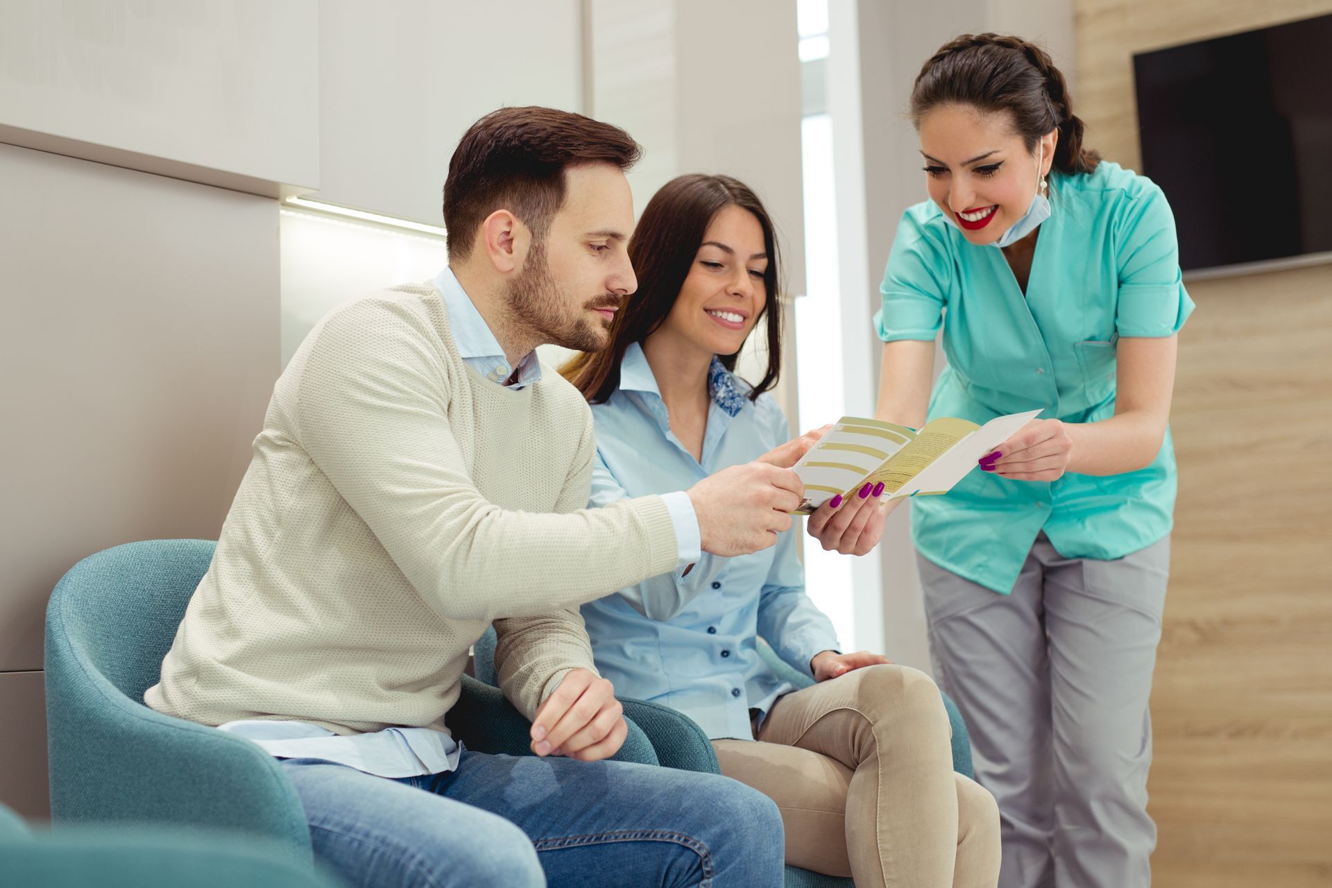 A man and a woman are sitting in a waiting room looking at a brochure and discussing finance options. 