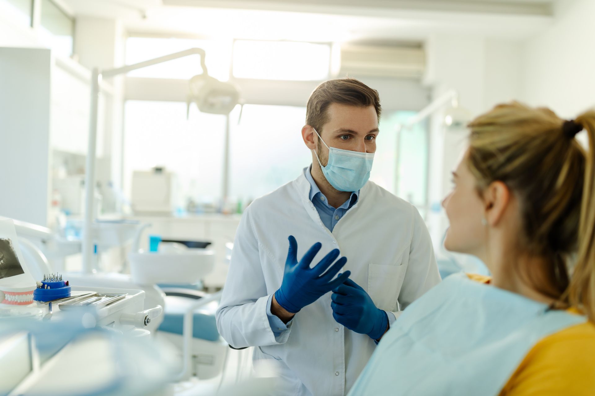A dentist wearing a mask and gloves is talking to a patient in a dental surgery.