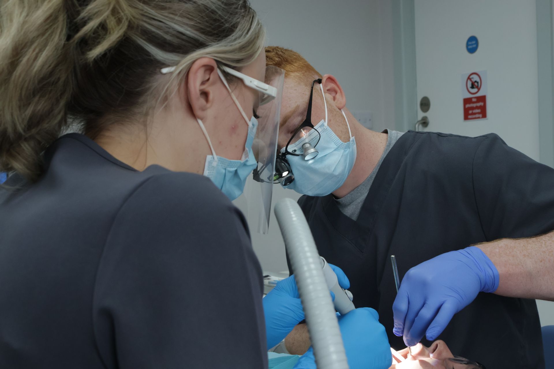 Two dentists are working on a patient 's teeth.. performing a scale and polish