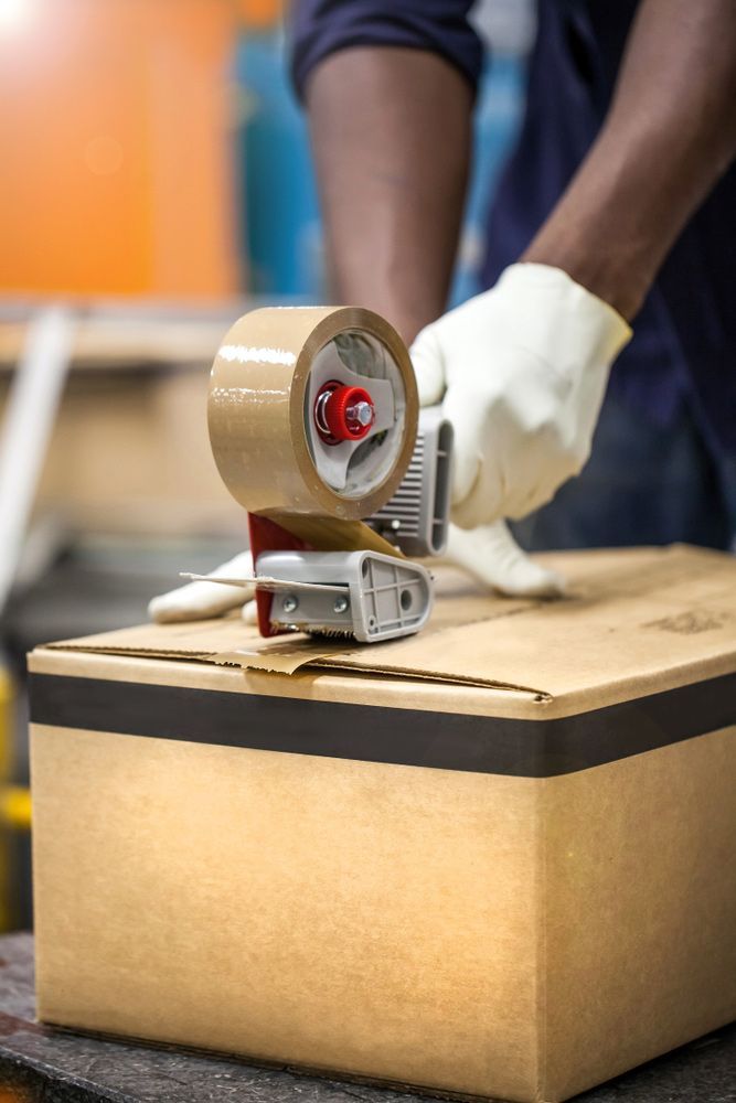 A Man Is Taping a Cardboard Box with Brown Tape — Bondi Removals and Taxi Trucks in Sydney, NSW