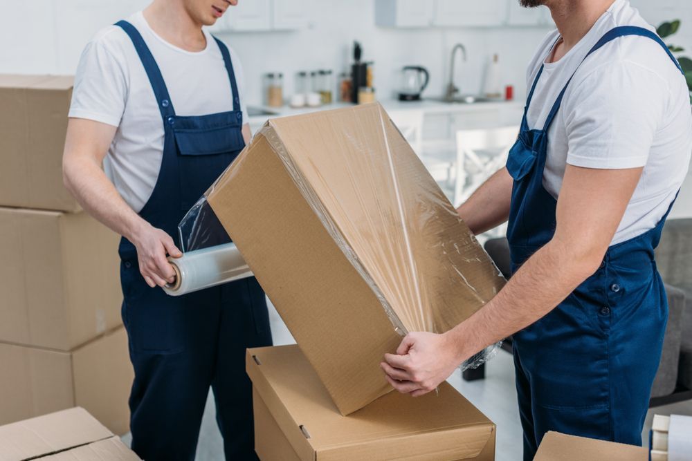 Two Men Are Wrapping a Cardboard Box With Plastic Wrap — Bondi Removals and Taxi Trucks In Dover Heights, NSW