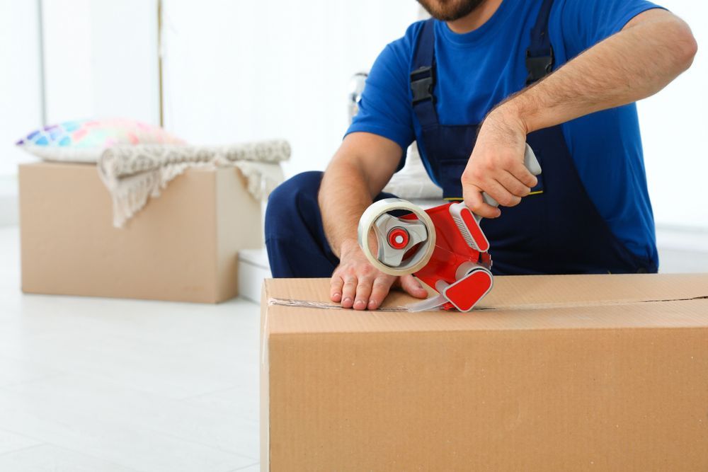 A Man is Sitting on a Box Using a Tape Dispenser — Bondi Removals and Taxi Trucks In Waverley, NSW