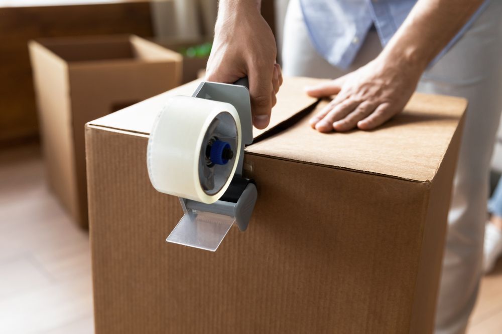 A Person Is Taping a Cardboard Box with Tape — Bondi Removals and Taxi Trucks in Randwick, NSW