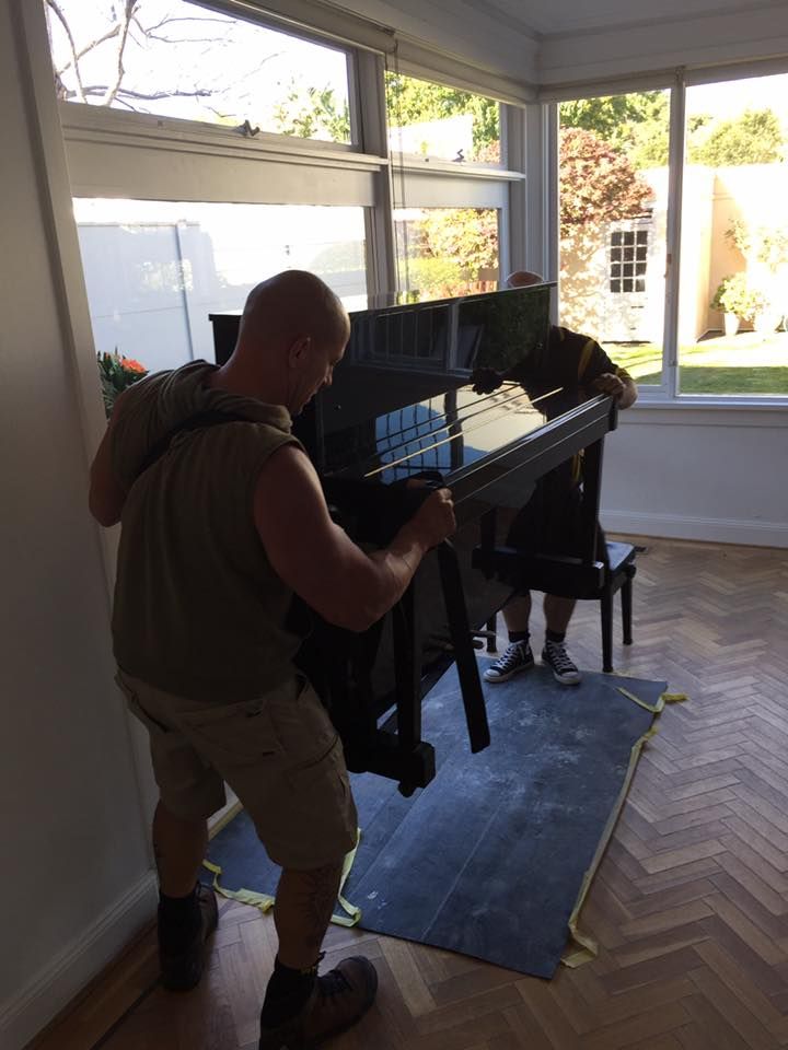 Two Men Are Carrying a Piano in A Living Room — Bondi Removals and Taxi Trucks in Randwick, NSW