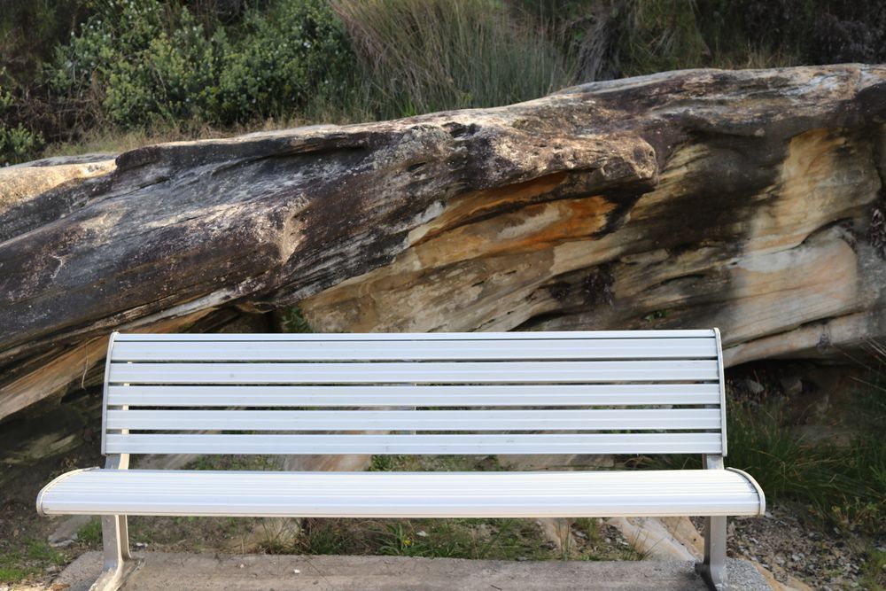 A White Bench Sits in Front of a Large Rock — Bondi Removals and Taxi Trucks in Bronte, NSW