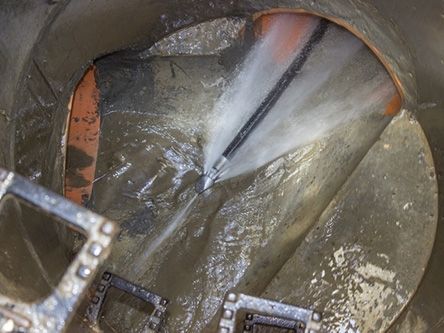 Person power-washing a circular metal tank interior with water spray and a ladder visible