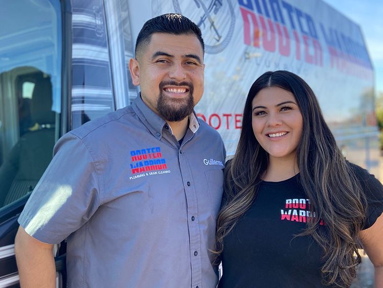 Two smiling employees in gray and black branded shirts stand beside a wrapped truck.