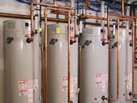 Row of large white industrial water heaters with copper pipes in a utility room