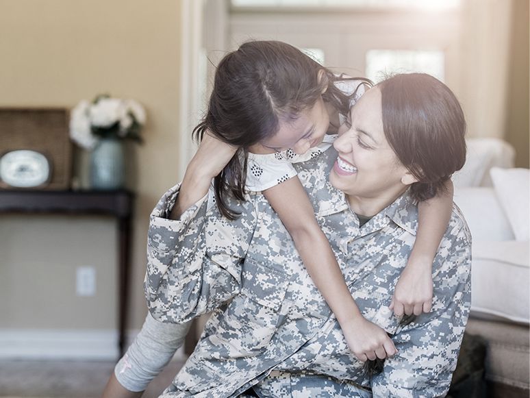 Soldier in camouflage hugging a smiling child indoors
