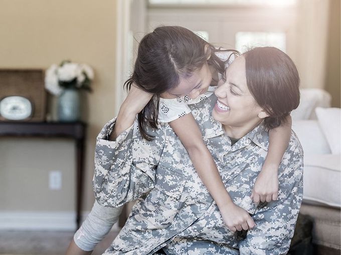 Smiling soldier in camouflage embracing a young child in a living room