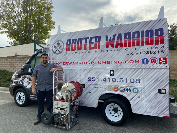 Man beside a Rooter Warrior plumbing service van with company logo and phone number displayed