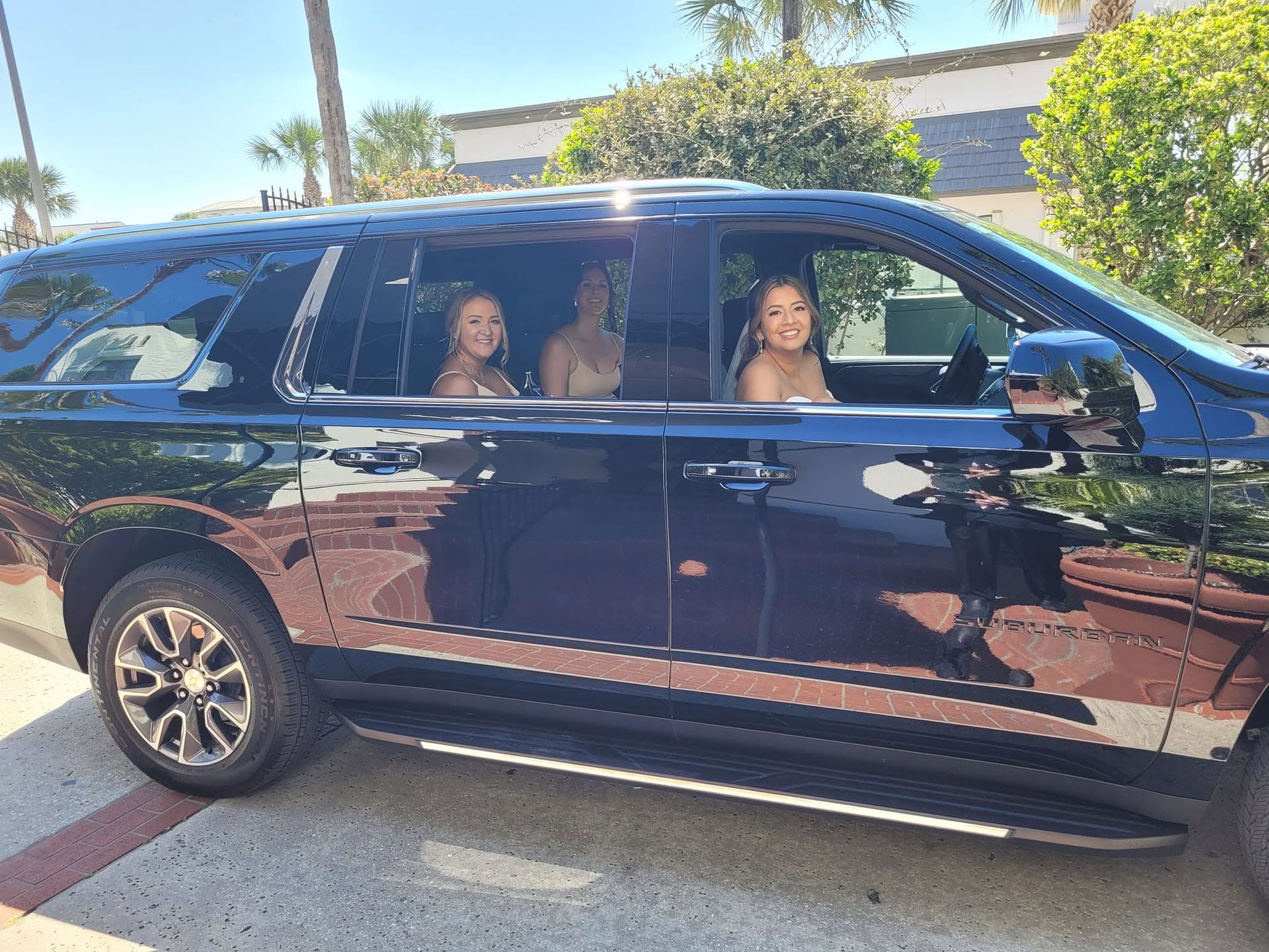 Black minivan parked curbside with three people visible through the windows on a sunny street