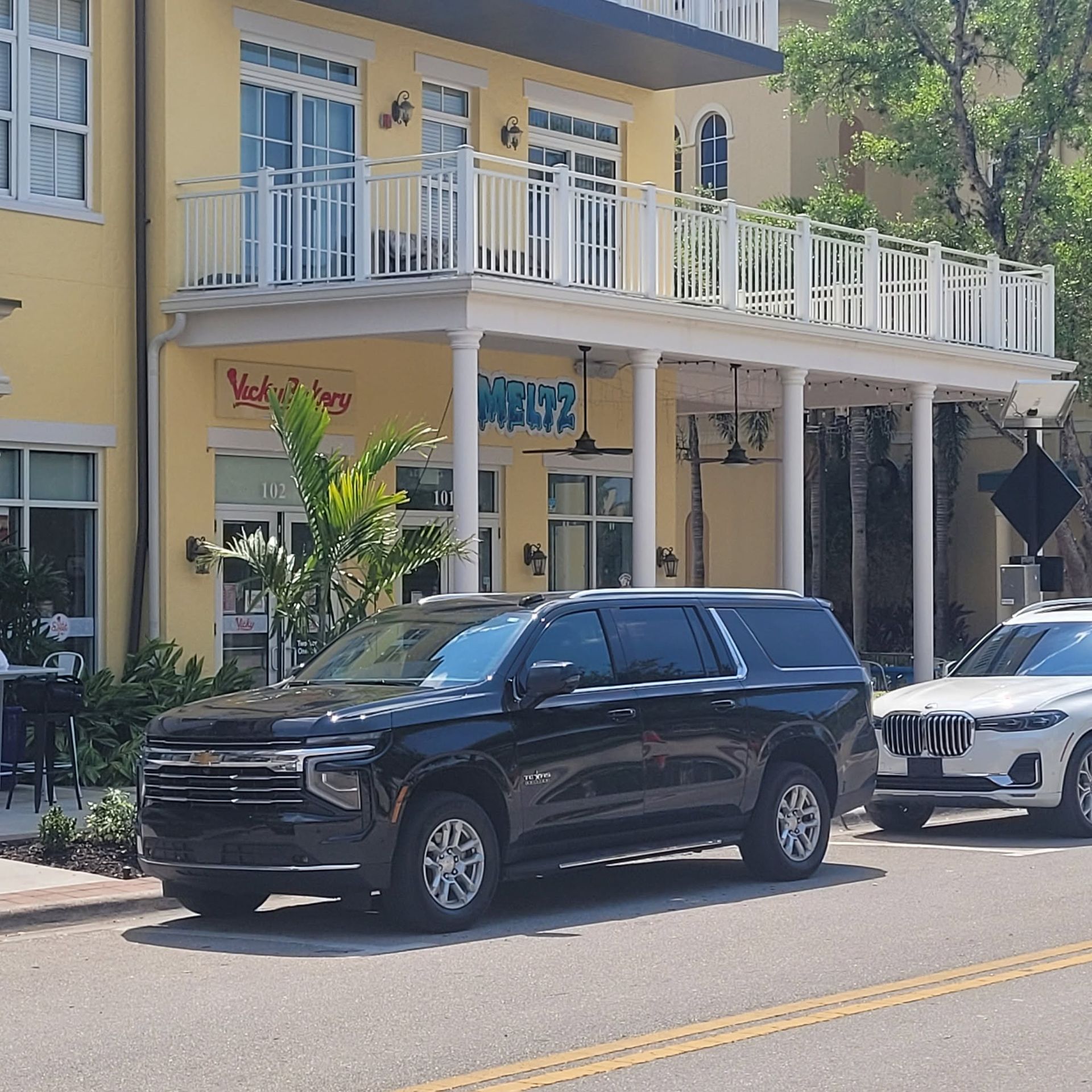 Black SUV parked on a sunny street beside a yellow building with white balcony railings.