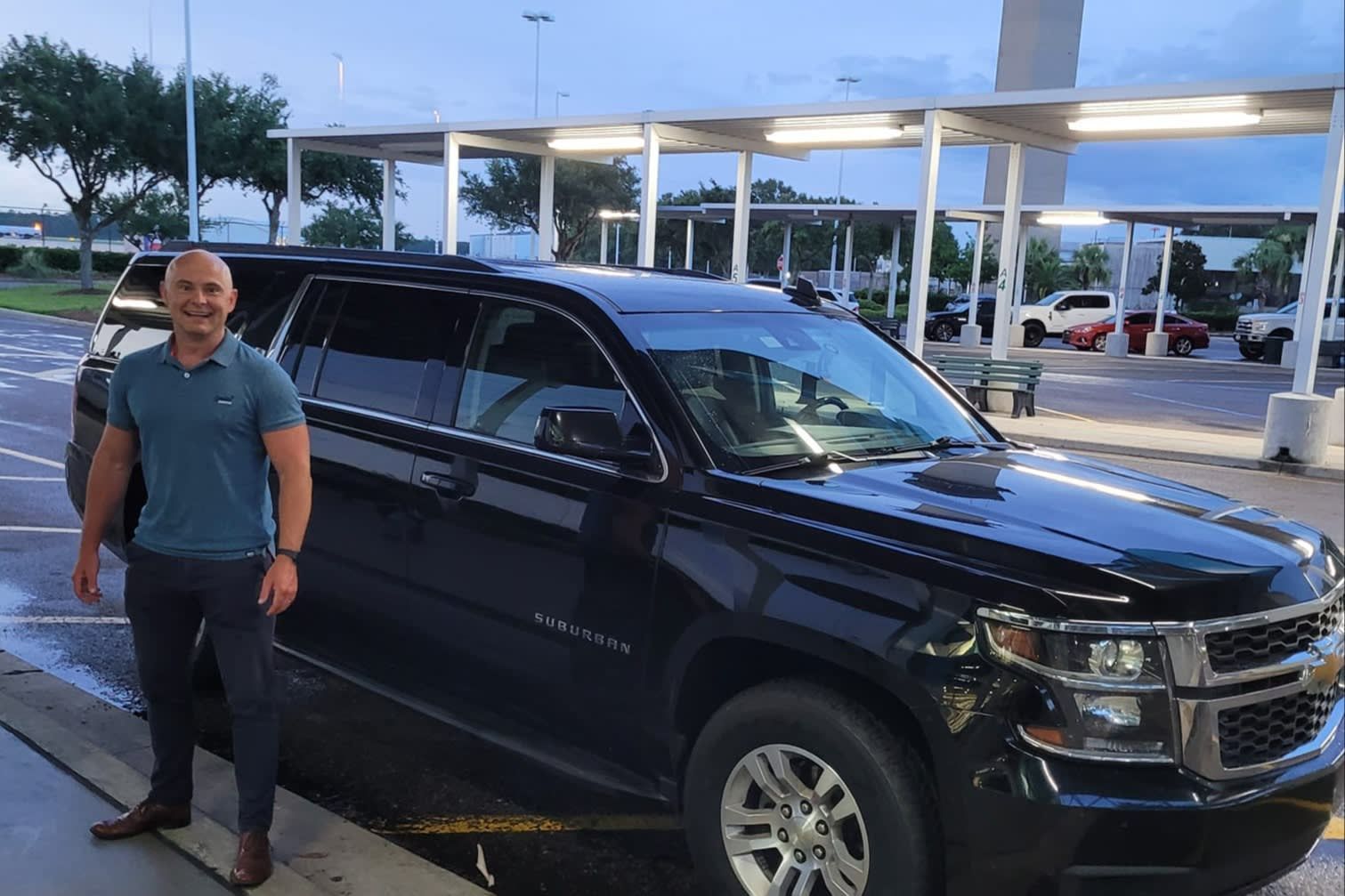 Man standing beside a black SUV at a gas station at dusk