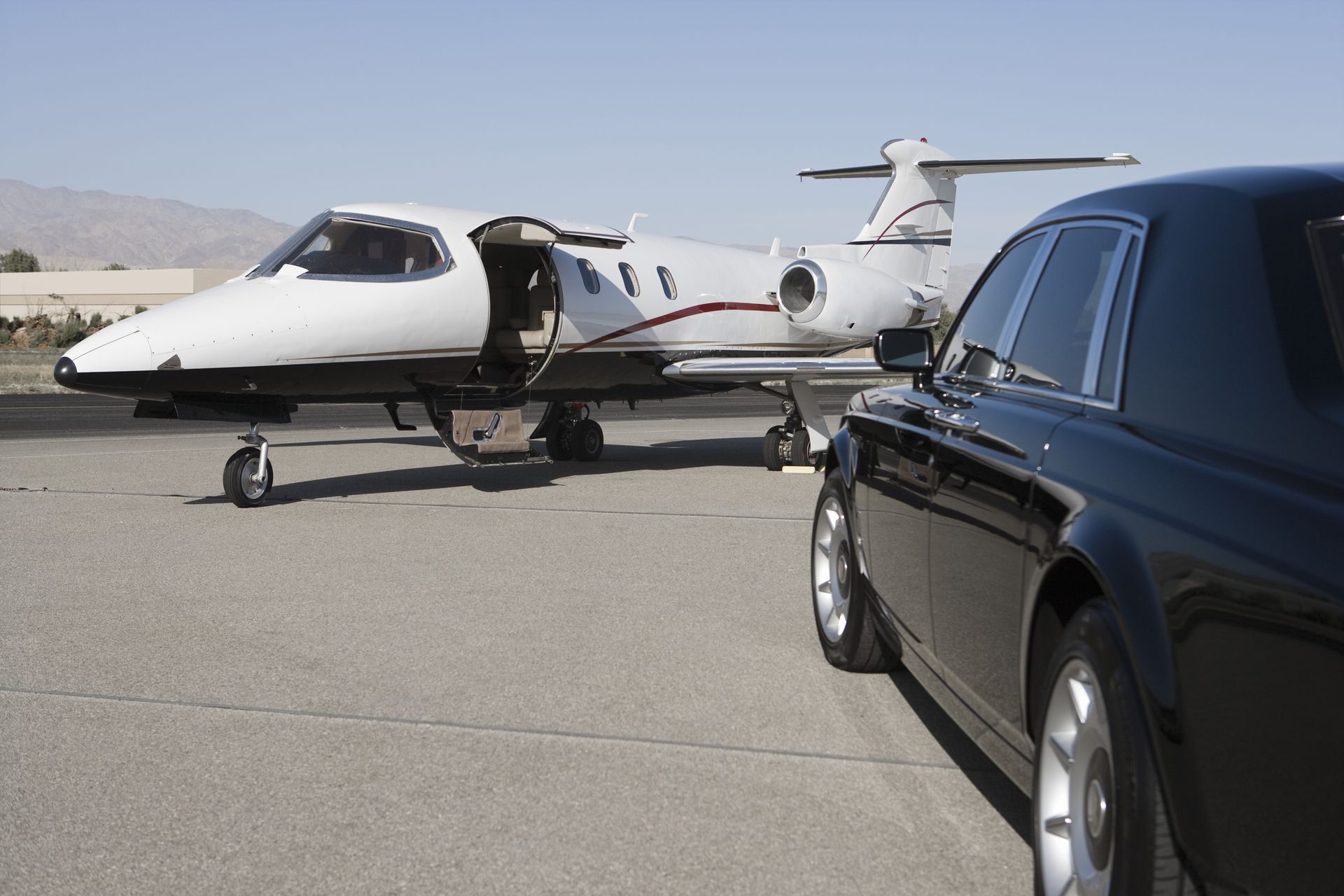 Private jet parked on runway beside a black luxury car in a desert airfield