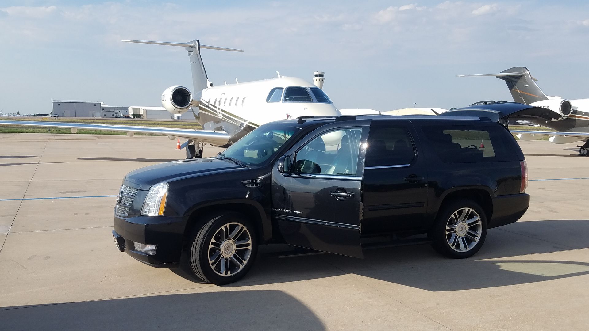 Black SUV parked on an airport tarmac in front of a white private jet.