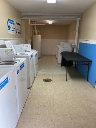 Laundry room with multiple white washing machines, black table, and water heater.