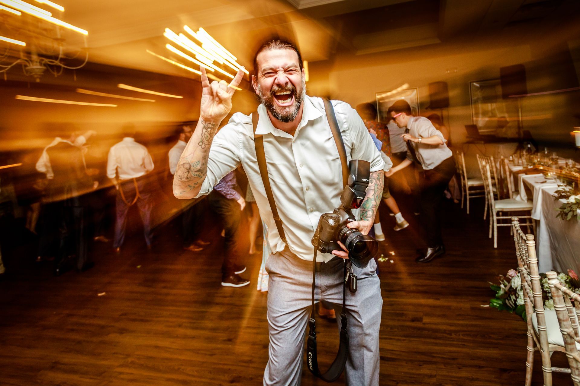 Man smiling and playing accordion at a lively indoor event with motion-blurred dancers in the background