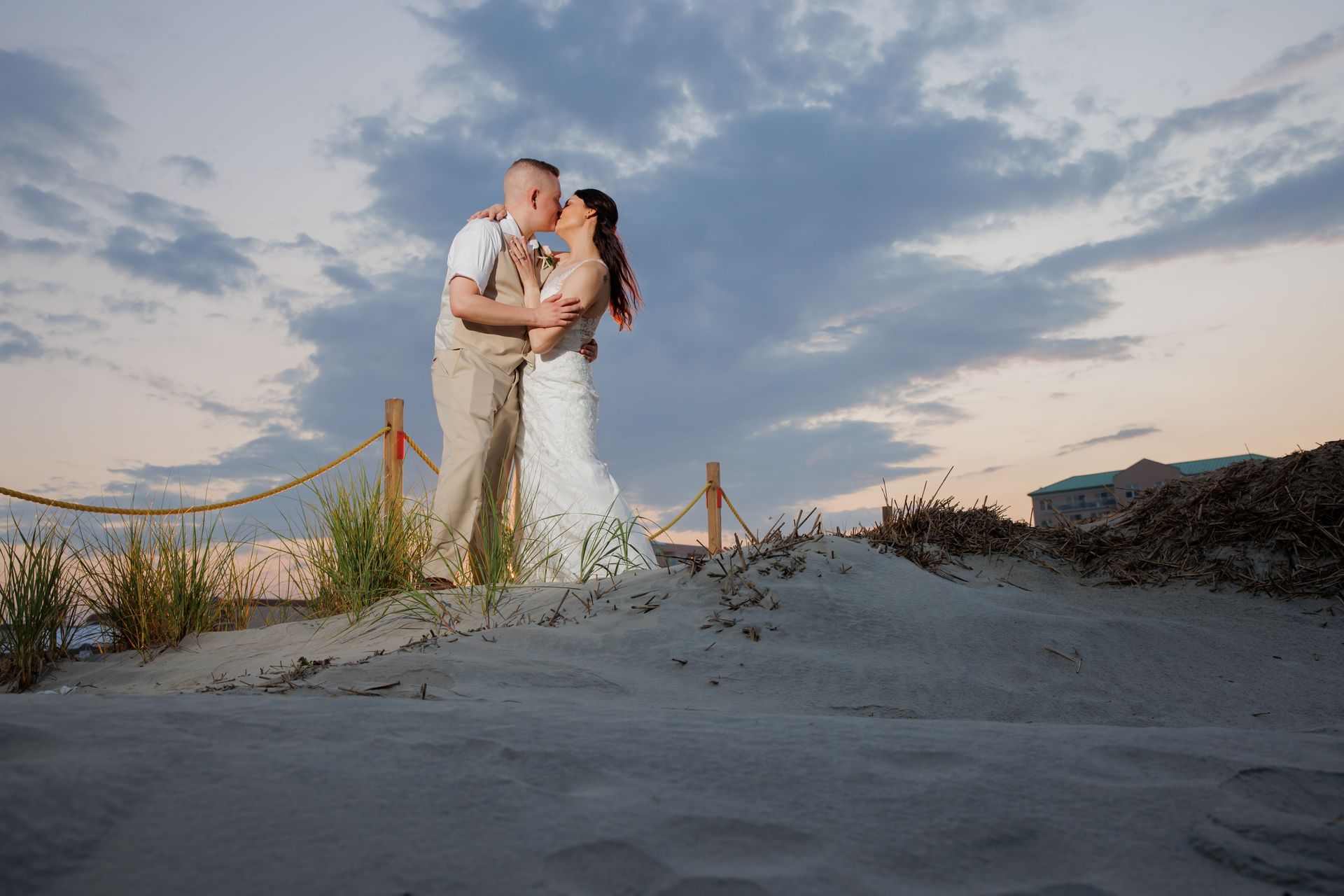 Bride and groom embracing on a sandy beach at sunset with pastel clouds
