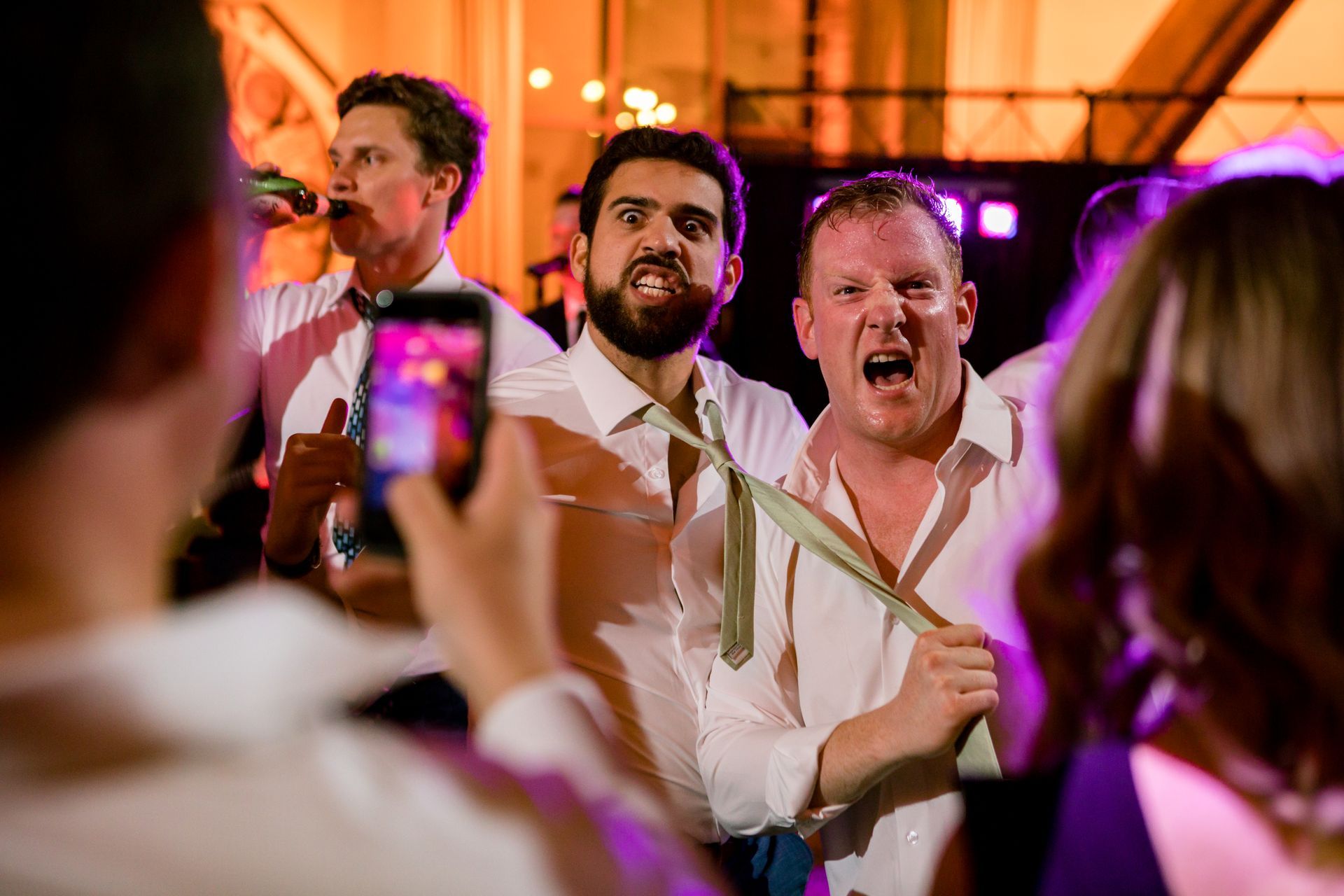Musicians performing at a lively indoor event while guests record them with phones