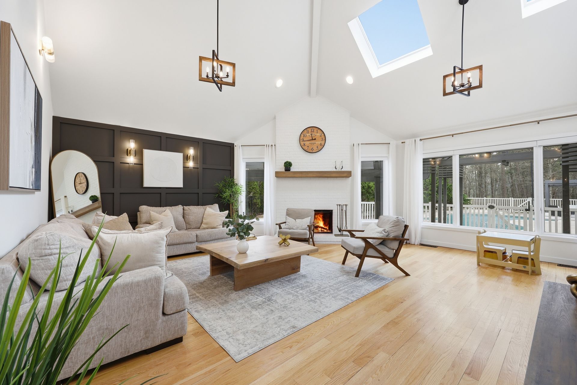 Bright, modern living room with white sofas, wood floors, skylights, fireplace, and large windows.