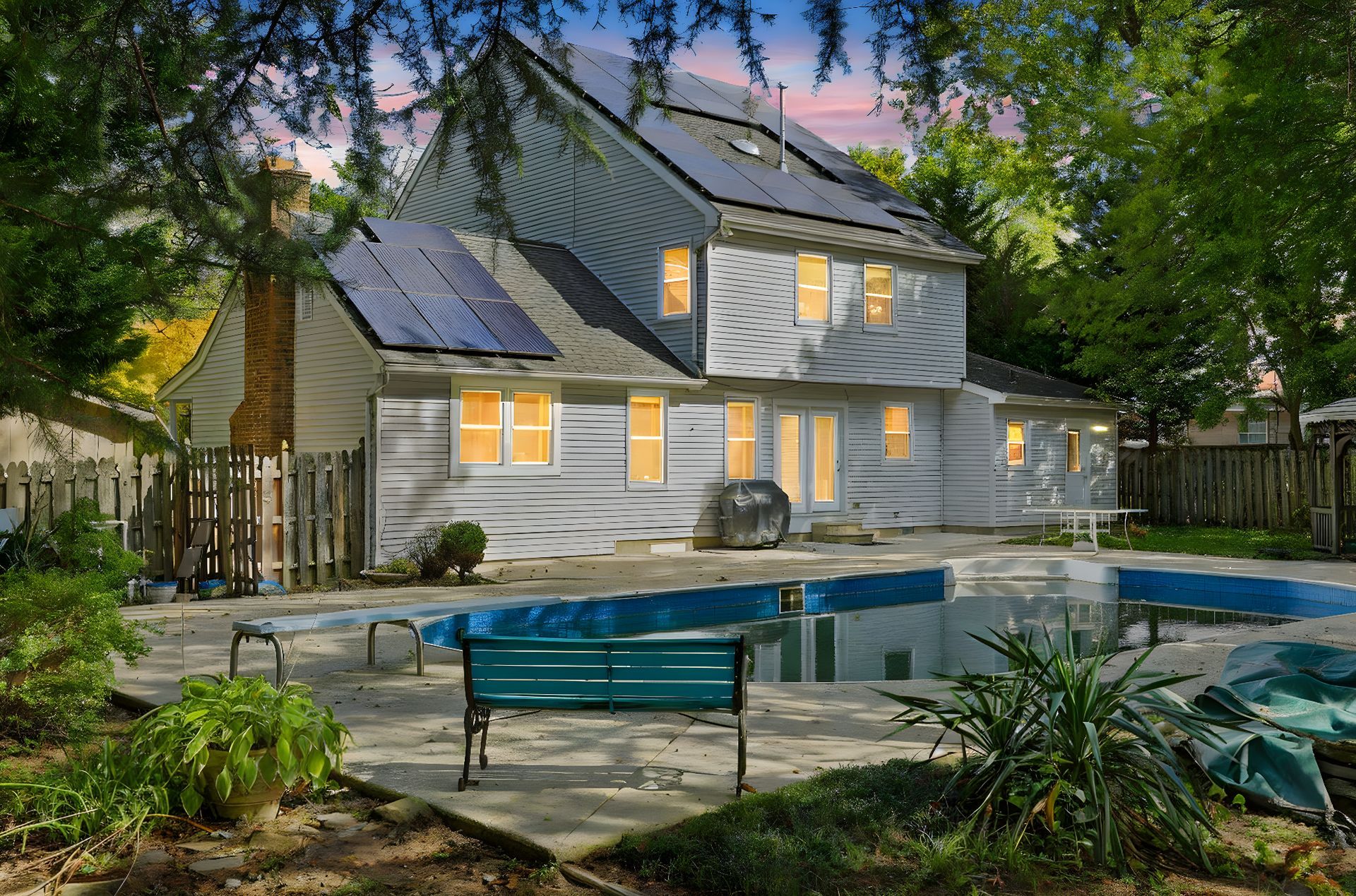 House with lit windows beside a backyard pool at dusk