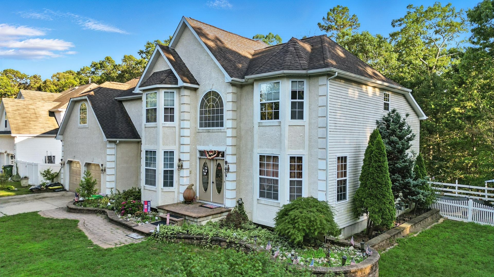 White two-story suburban house with tall windows, gabled roof, and a green front lawn