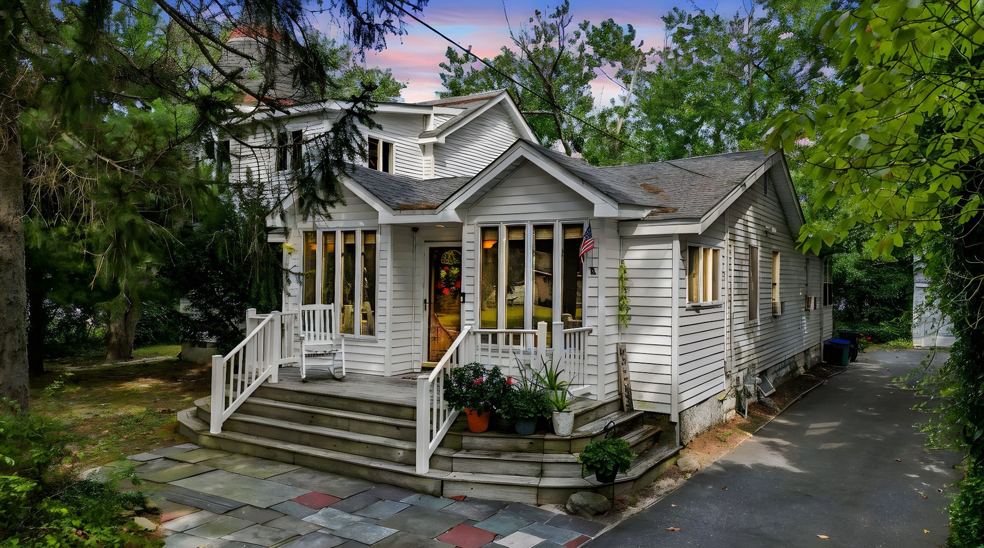 Charming white cottage with front porch, yellow door, and stone steps along a tree-lined driveway