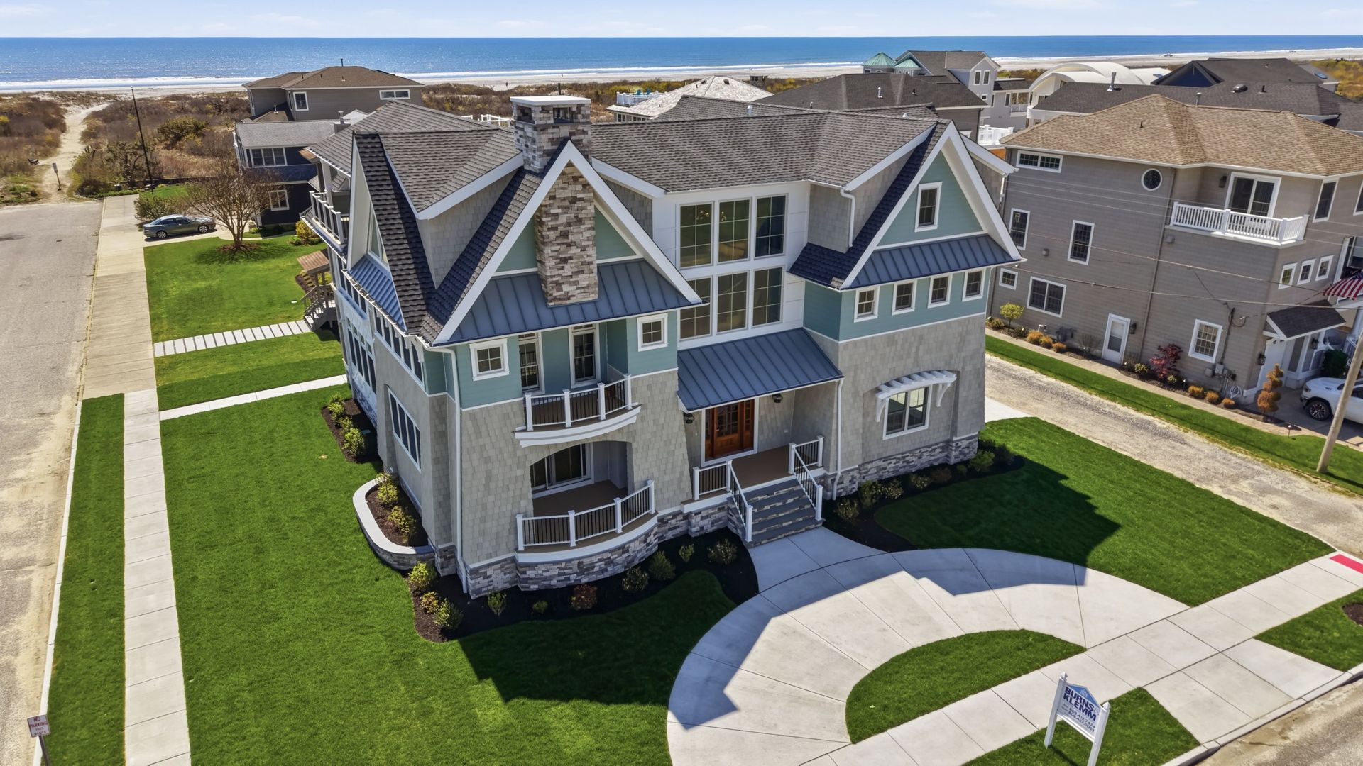 Large gray and blue suburban house with a manicured lawn and curved driveway near the coast