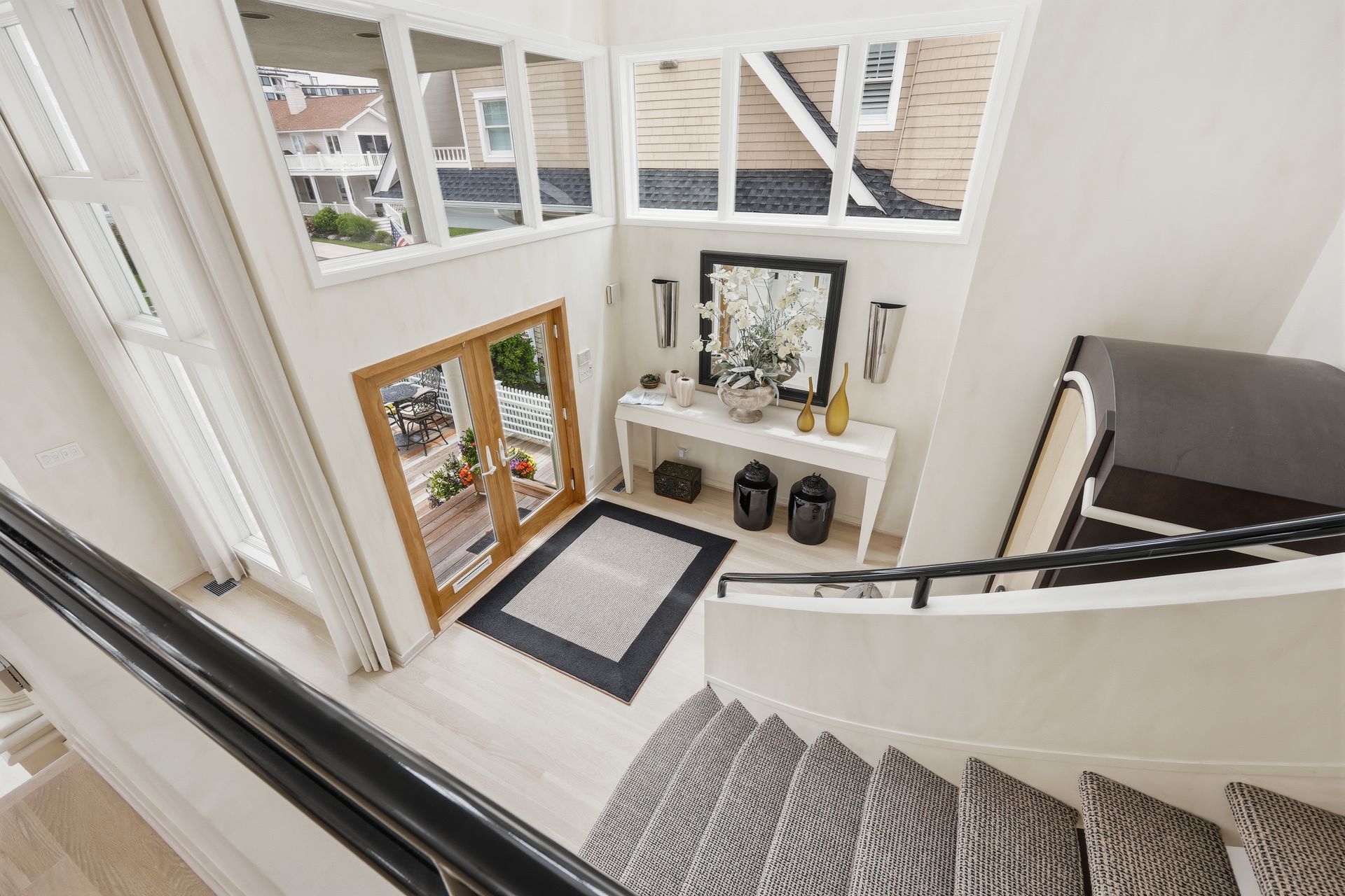 Bright entryway with white staircase, wooden front door, mirror console, and black-and-white rug.