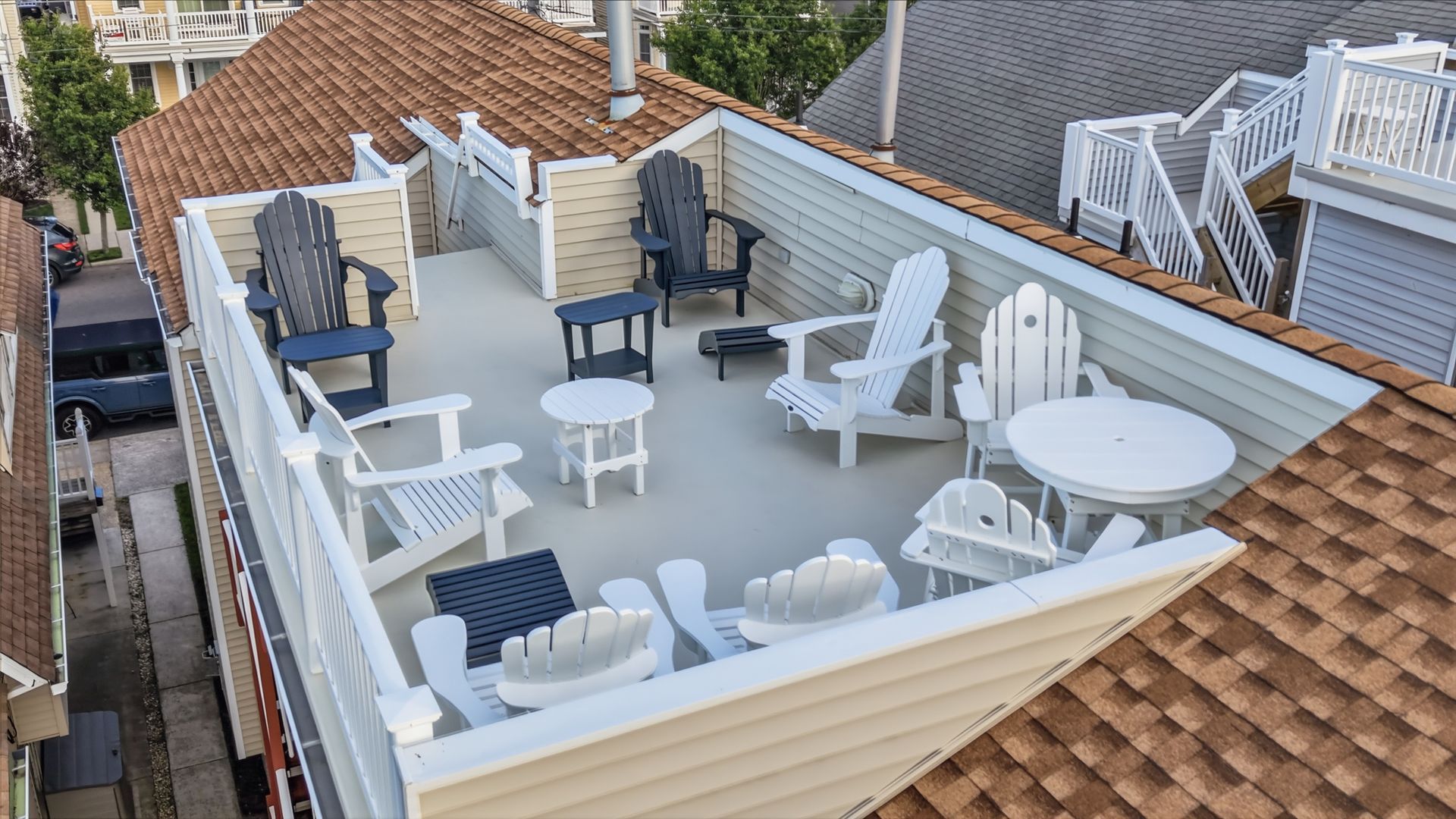 Rooftop patio with white furniture and blue cushions, surrounded by tan siding and red shingle roofs