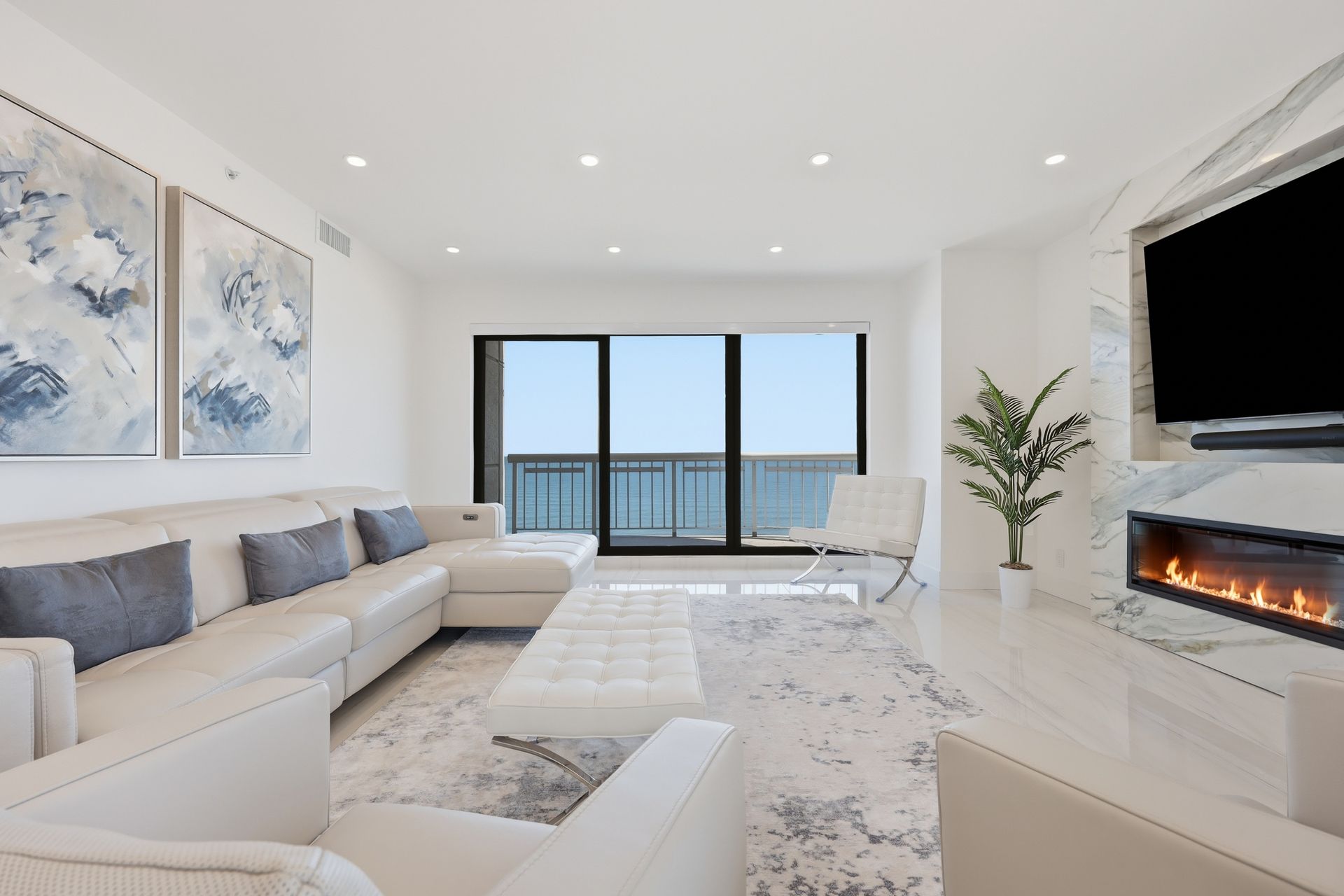 Bright modern living room with white sectional, fireplace, wall TV, and ocean-view balcony doors
