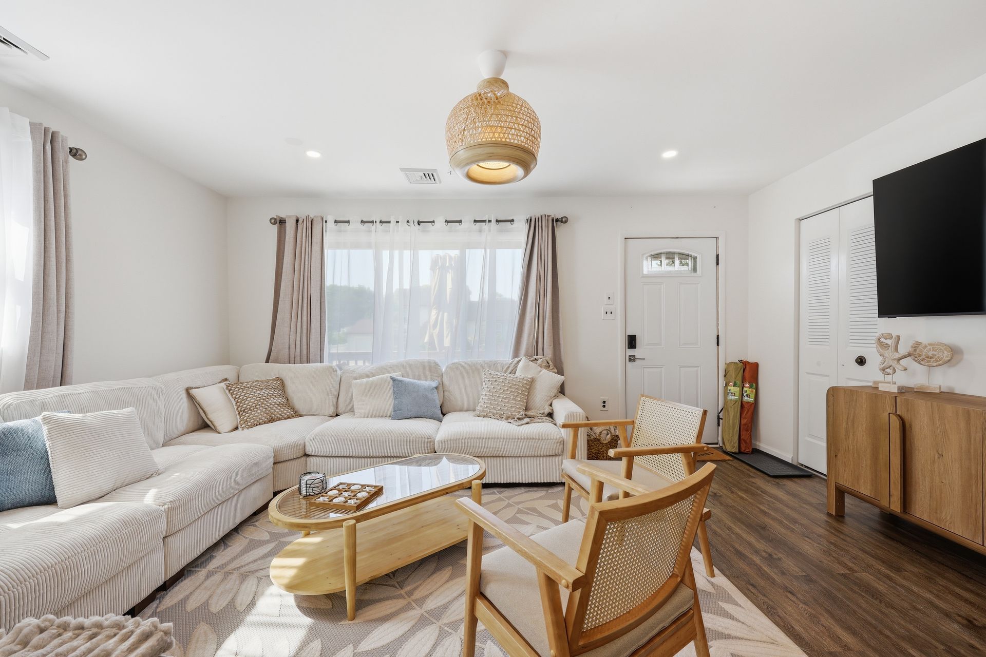 Bright living room with white sectional sofa, woven chairs, wooden TV console, and large window with curtains