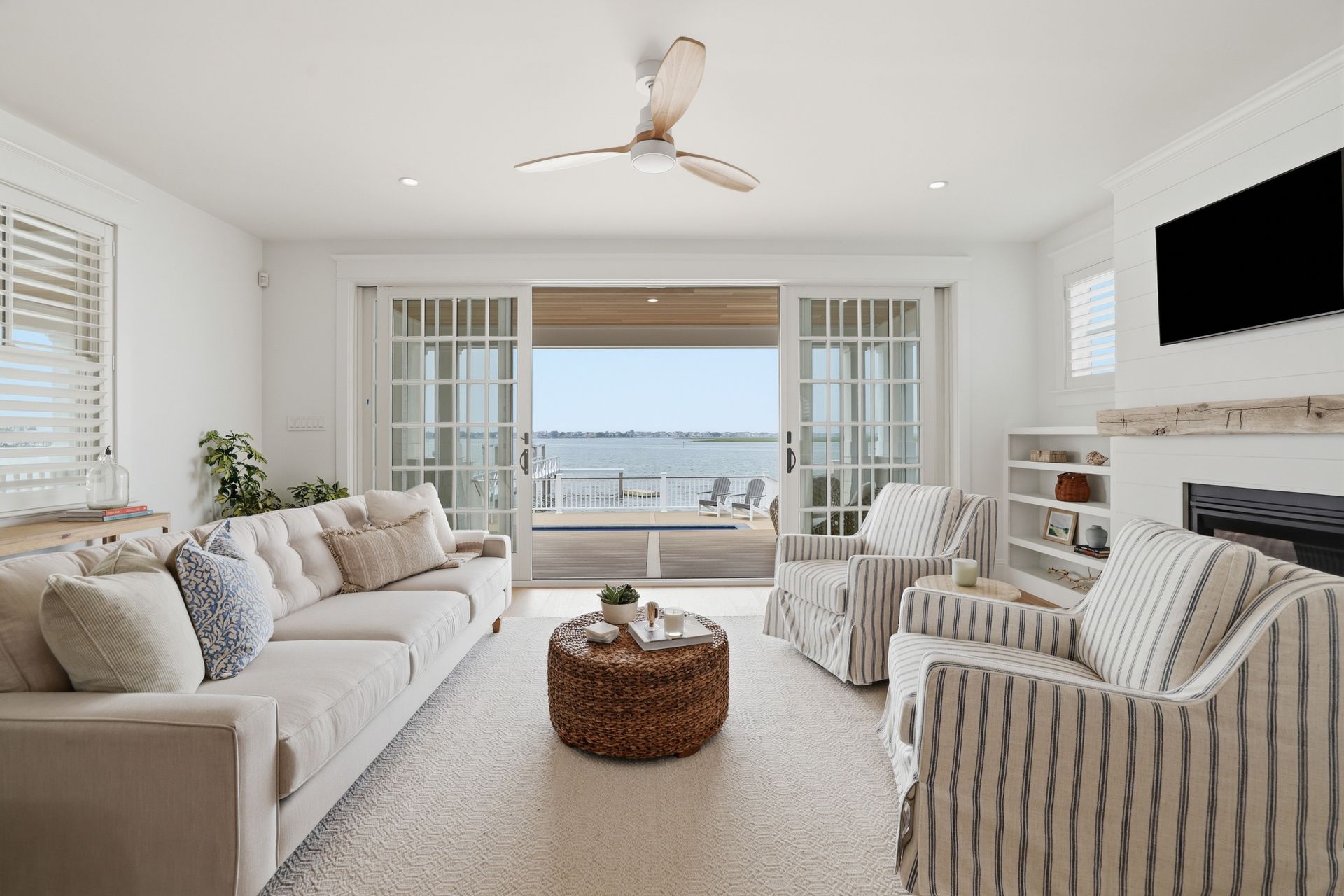Bright coastal living room with striped armchairs, a sofa, and ocean view through French doors.