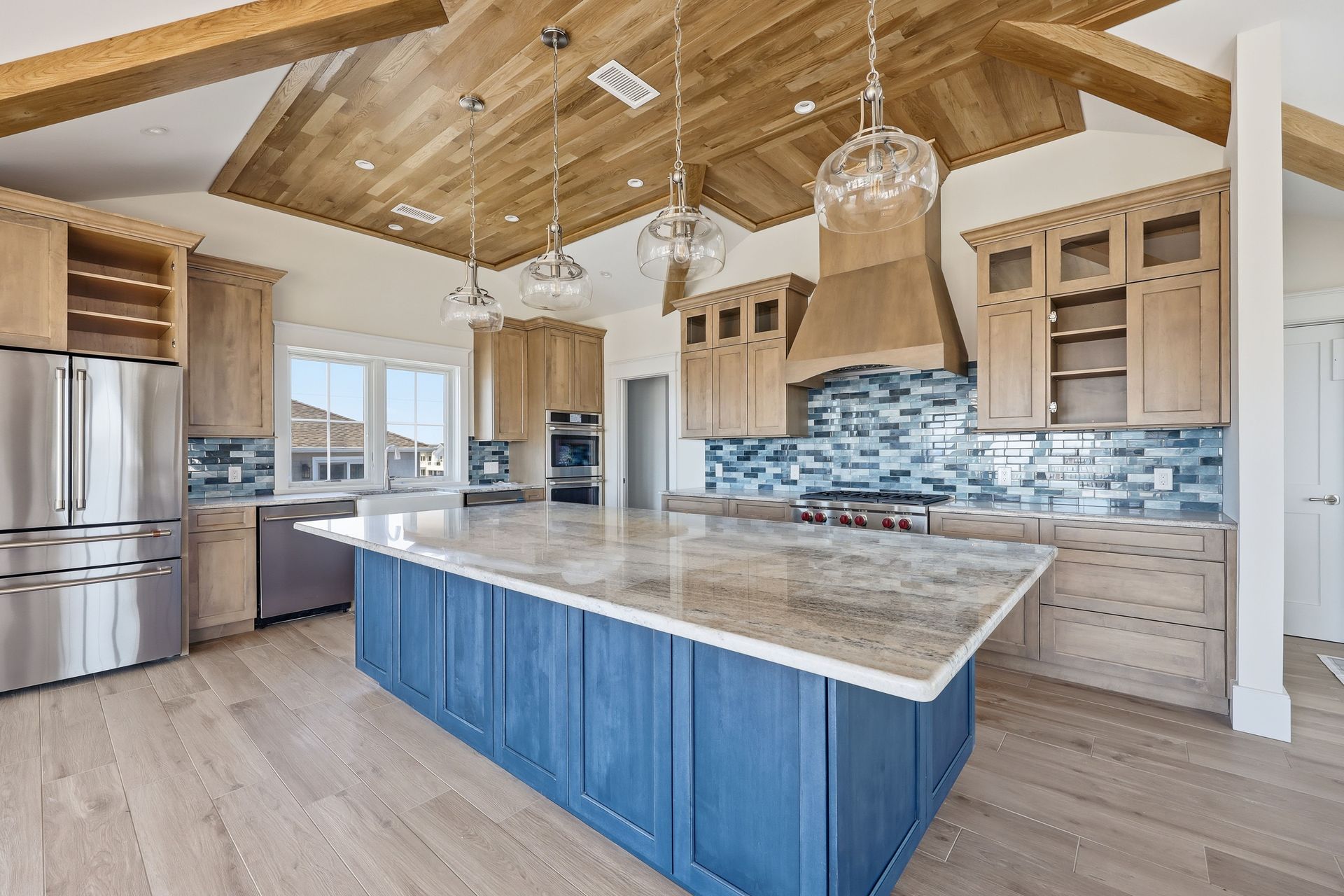 Modern kitchen with blue island, wood beams, stainless appliances, and tile backsplash