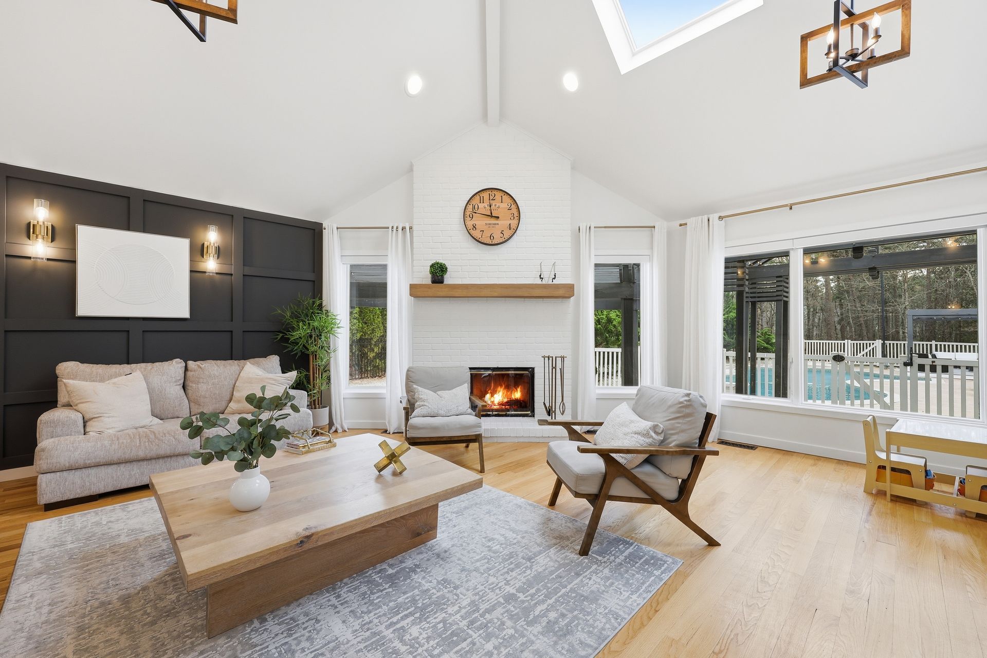Bright, modern living room with white vaulted ceiling, stone fireplace, beige sofa, and large windows.