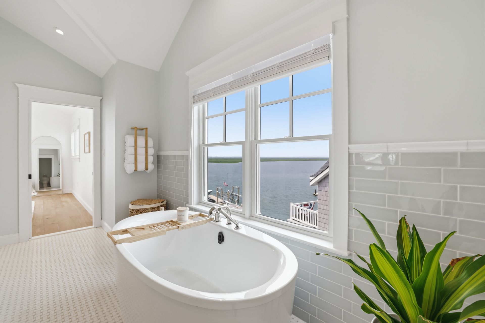Bright bathroom with a white soaking tub, large window view, and green potted plant.