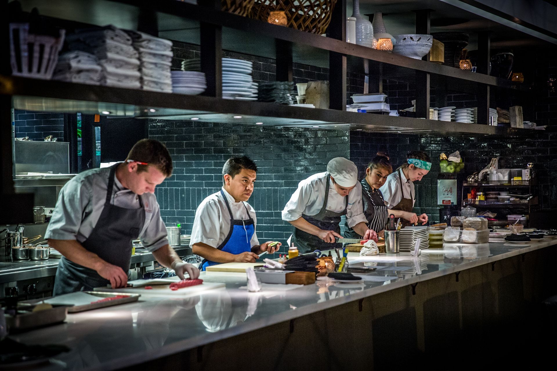 Chefs preparing food at a stainless-steel kitchen counter in a busy restaurant kitchen
