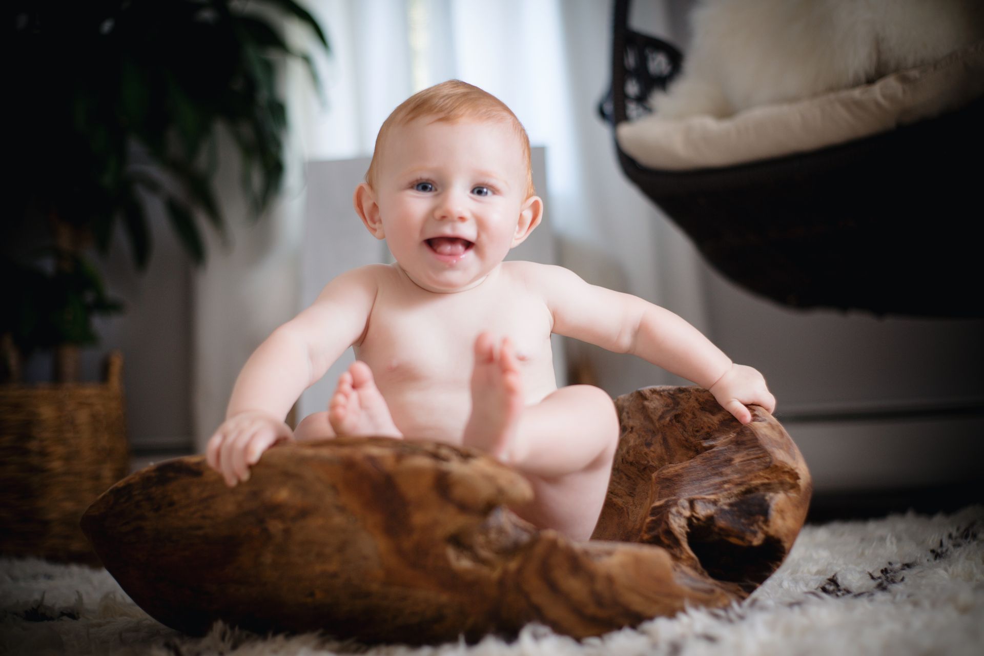 Smiling baby leaning on a wooden log on a soft rug indoors
