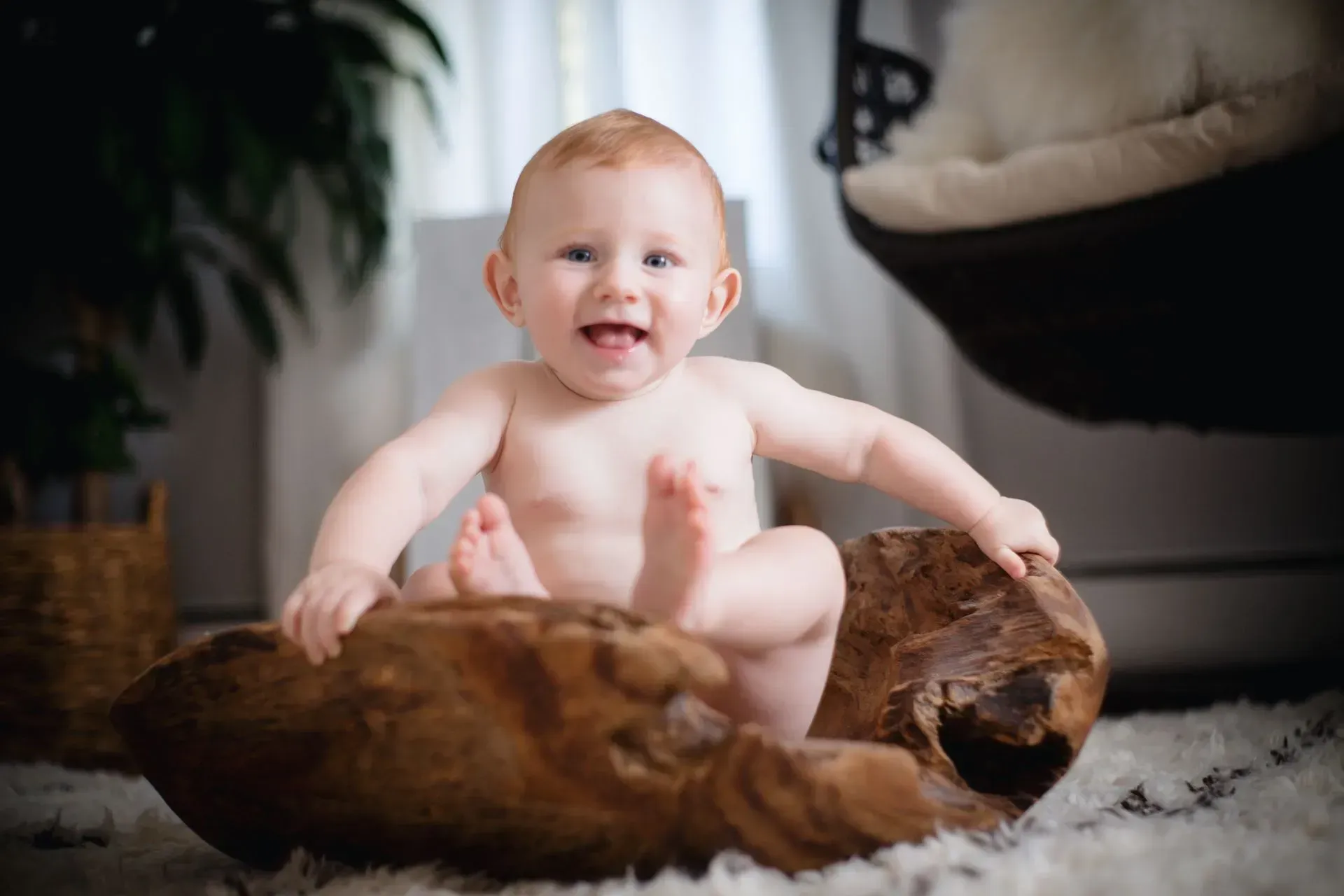 Smiling baby sitting on a brown fur rug with a stuffed dog toy in a cozy living room.