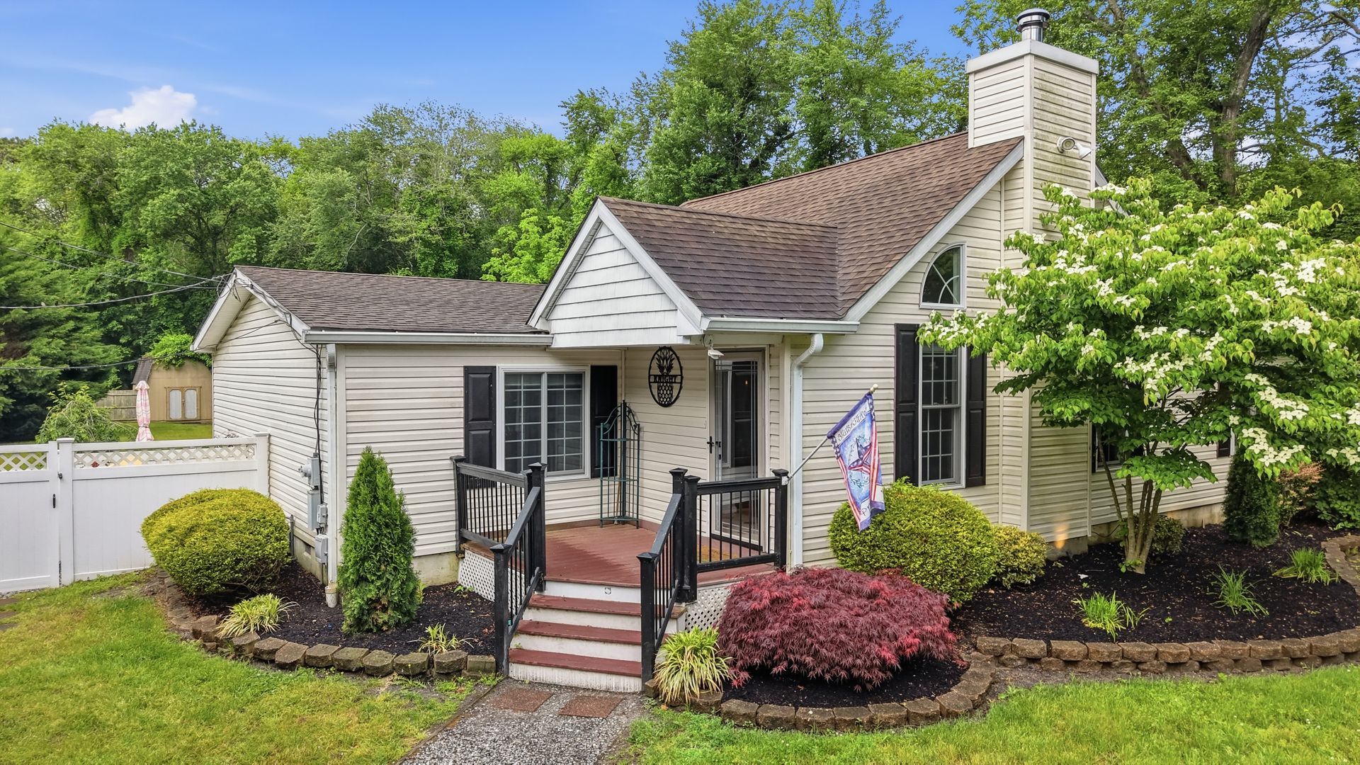 Small cream cottage with black shutters, brick steps, and a landscaped front yard