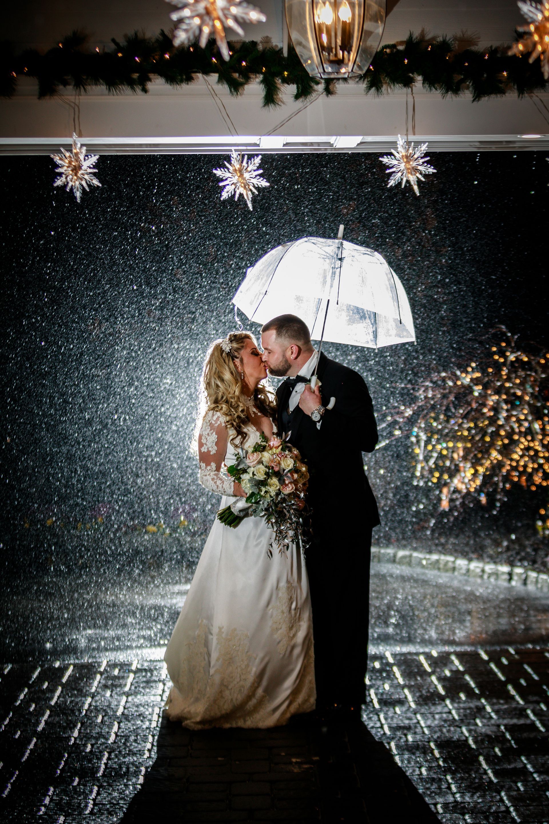 Couple kissing under a clear umbrella in the rain at a decorated wedding venue at night