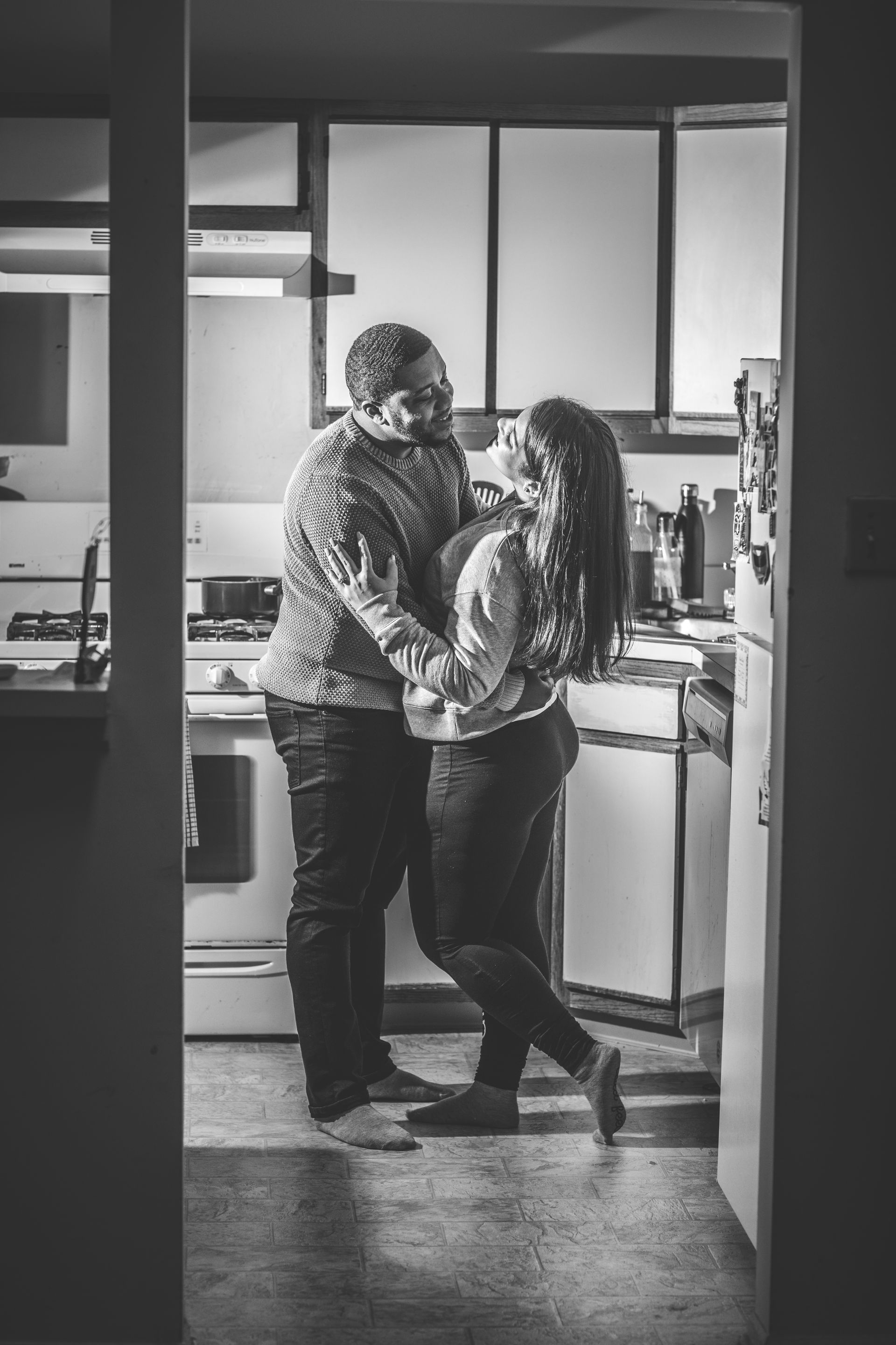 A couple standing close and embracing in a kitchen, shown in black and white.