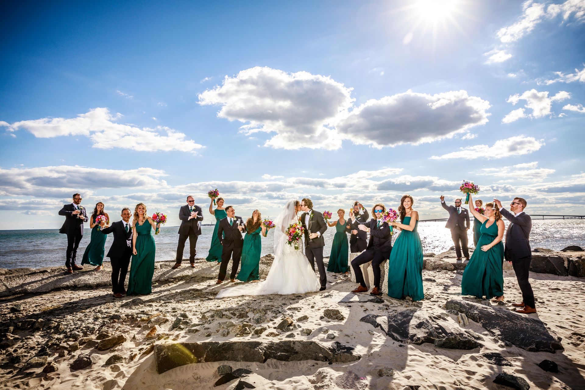 Wedding party posing on a rocky beach under a bright sky with the ocean in the background