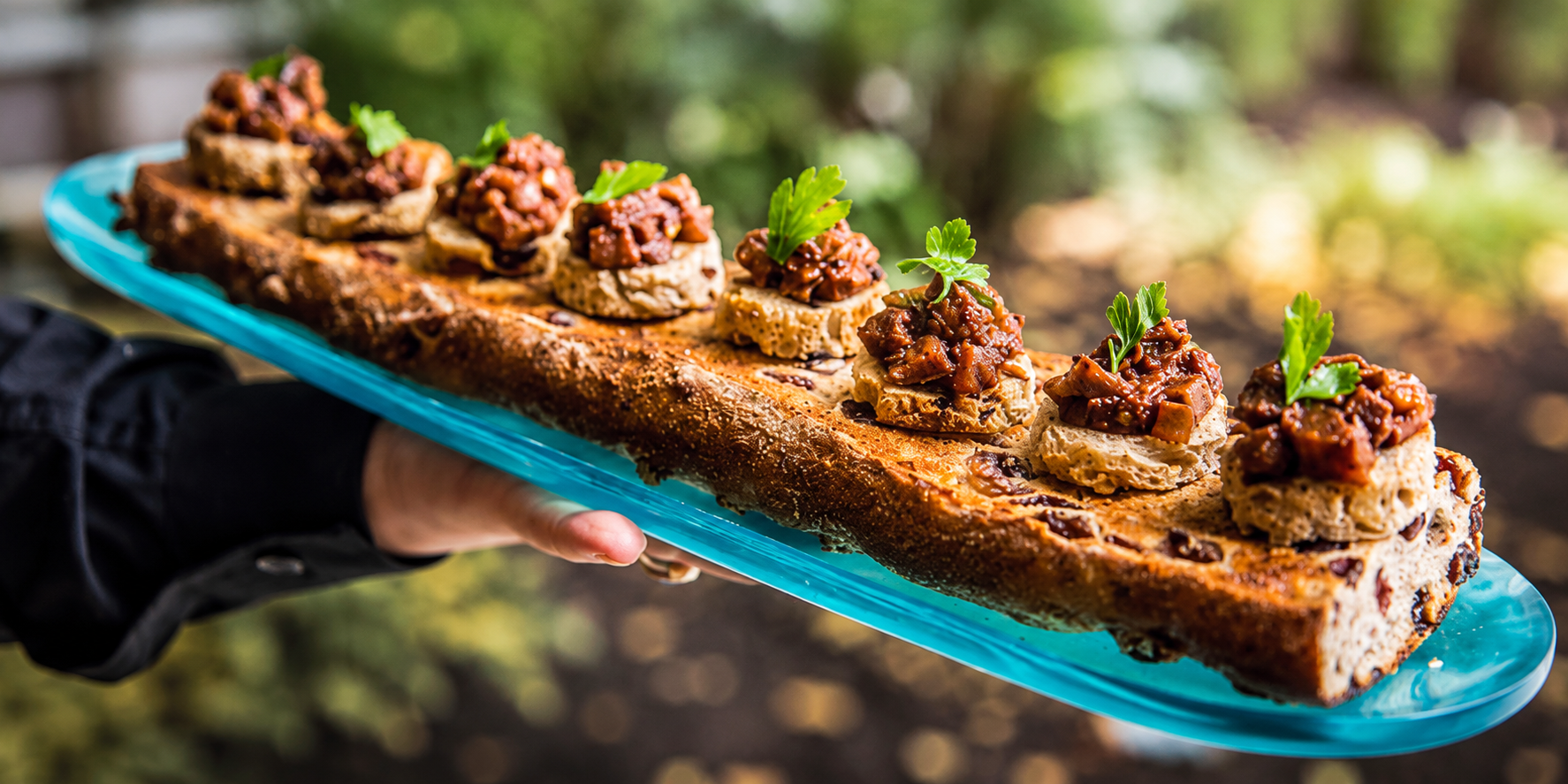 Hand-held blue platter with sliced rustic bread topped with mushrooms and herbs