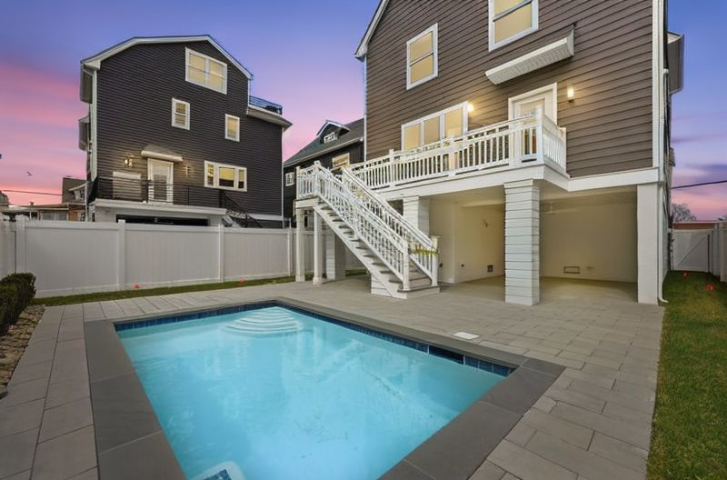 Backyard with a small in-ground pool beside a staircase leading to a raised deck and house.