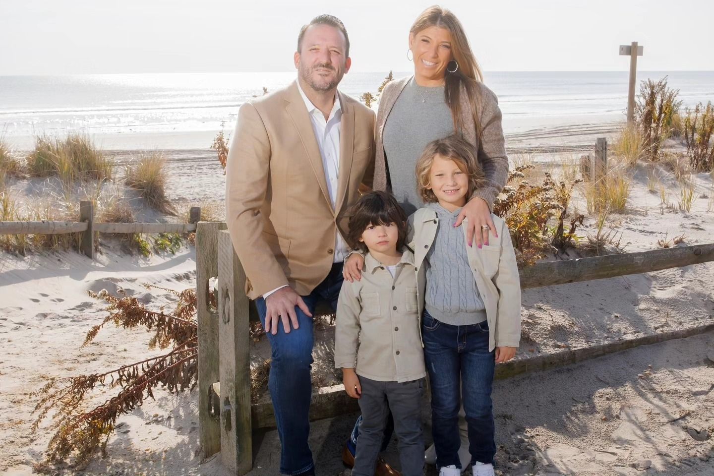 Family standing on a beach near wooden fencing, with ocean waves in the background.