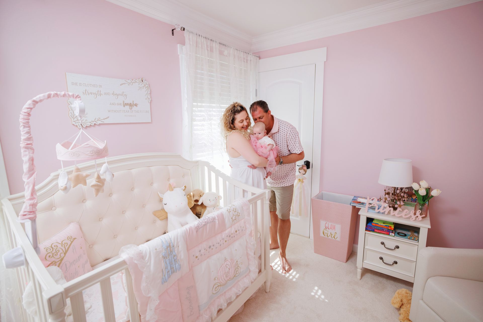 Pink nursery with crib, dresser, and a couple standing near the window